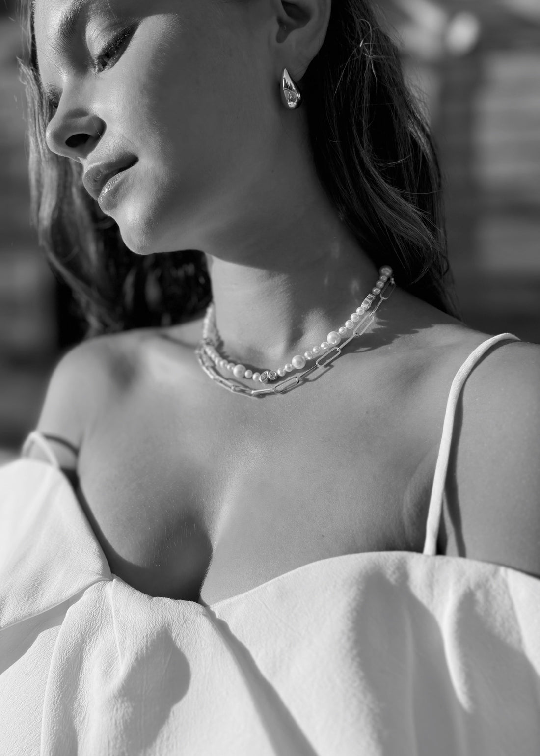Close up look on timeless jewelry mixing silver and pearl necklace with bold minimalist silver earrings. Embodying soft elegance and timelessness