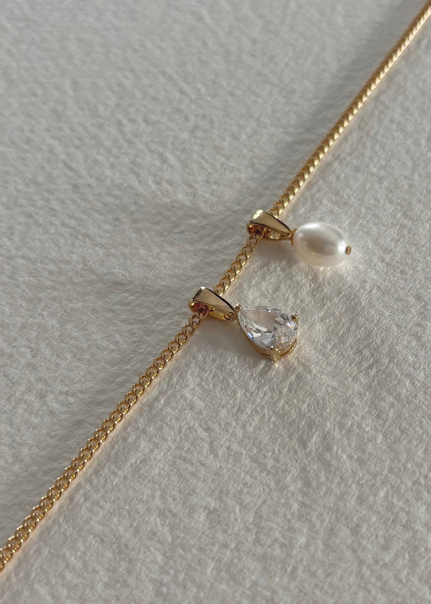Gold necklace adorned with semi-precious stones and a delicate pearl pendant, featuring a timeless design that reflects modern elegance, refined simplicity, and soft luminous shine.